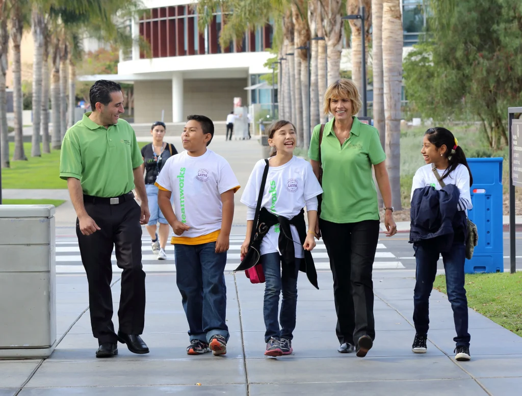 Two counselors and 3 kids walking down a sidewalk talking and laughing