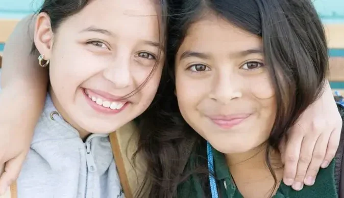 two girls hugging and smiling at the camera